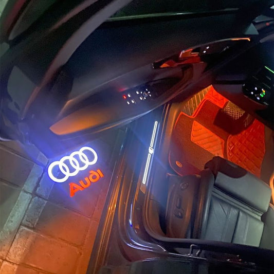 Door welcome light projecting a logo onto the ground next to an open car door at night
